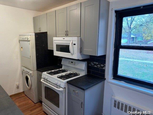 kitchen with backsplash, stacked washing maching and dryer, radiator, white appliances, and hardwood / wood-style floors