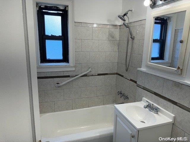 bathroom featuring tiled shower / bath combo, tile walls, and vanity