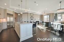 kitchen featuring pendant lighting, a raised ceiling, sink, an island with sink, and stainless steel refrigerator