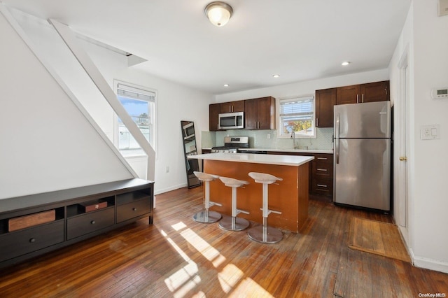 kitchen with dark hardwood / wood-style floors, a kitchen island, stainless steel appliances, and a breakfast bar