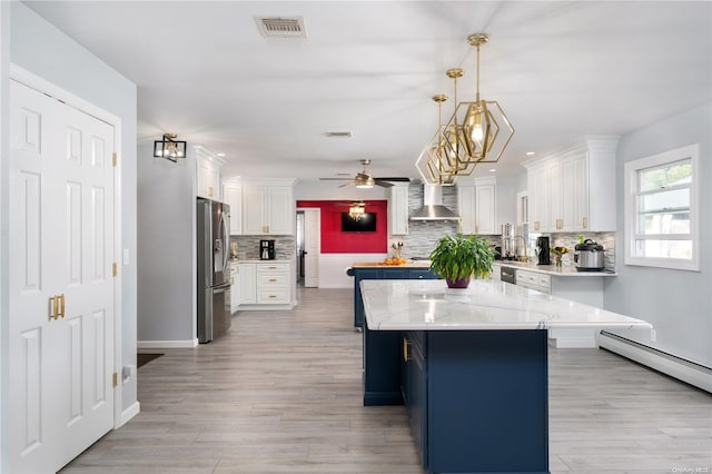 kitchen with a center island, hanging light fixtures, wall chimney exhaust hood, stainless steel fridge, and white cabinetry