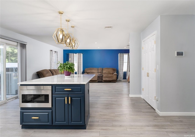 kitchen featuring blue cabinets, light hardwood / wood-style flooring, light stone countertops, decorative light fixtures, and a kitchen island