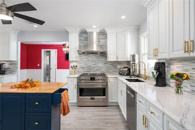 kitchen featuring butcher block counters, white cabinetry, sink, wall chimney range hood, and appliances with stainless steel finishes