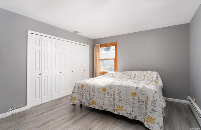 bedroom featuring baseboard heating, a closet, and light hardwood / wood-style flooring