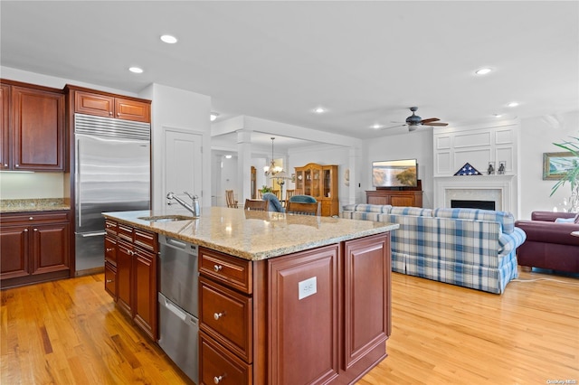 kitchen featuring sink, decorative light fixtures, stainless steel built in fridge, a center island with sink, and light wood-type flooring