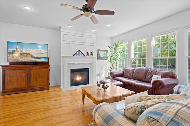 living room with a fireplace, light wood-type flooring, and ceiling fan