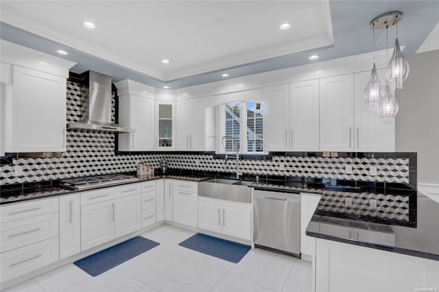 kitchen with decorative backsplash, appliances with stainless steel finishes, wall chimney range hood, decorative light fixtures, and white cabinets