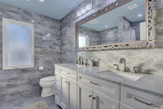 bathroom with vanity, toilet, tile walls, and a wealth of natural light