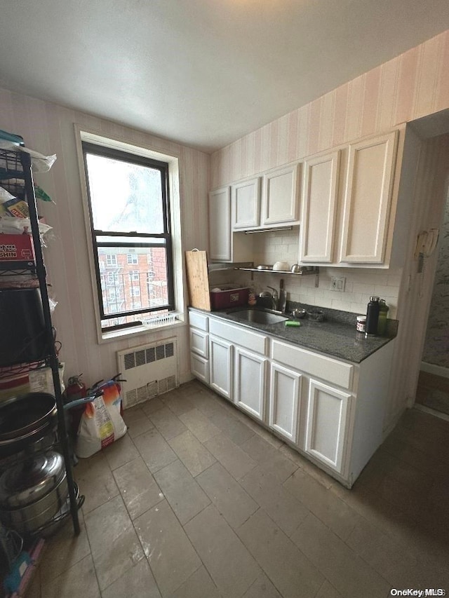 kitchen featuring backsplash, white cabinetry, radiator, and sink