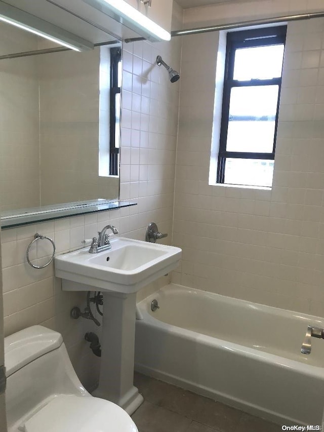 bathroom featuring tiled shower / bath combo, tile patterned flooring, backsplash, toilet, and tile walls