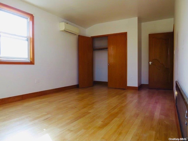 unfurnished bedroom with a wall mounted AC, a closet, and hardwood / wood-style floors