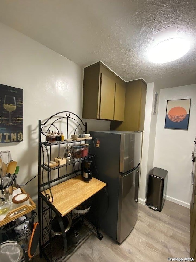 kitchen featuring stainless steel refrigerator, a textured ceiling, and light wood-type flooring