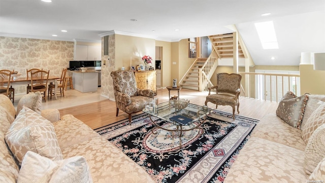 living room with crown molding, vaulted ceiling with skylight, and light hardwood / wood-style floors