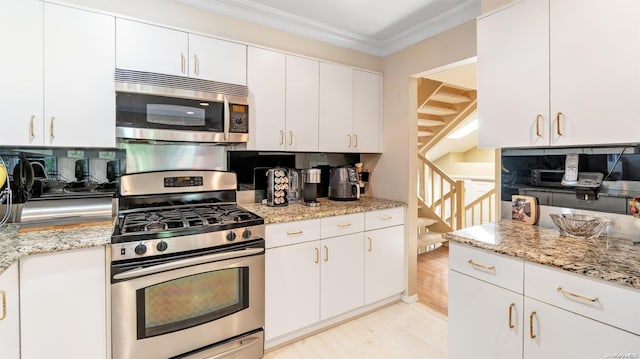 kitchen with light stone countertops, appliances with stainless steel finishes, ornamental molding, white cabinets, and light hardwood / wood-style floors