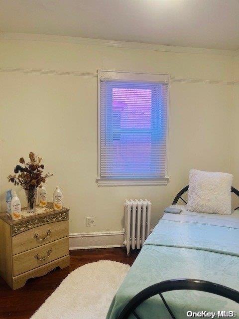 bedroom with dark hardwood / wood-style flooring, radiator, and ornamental molding