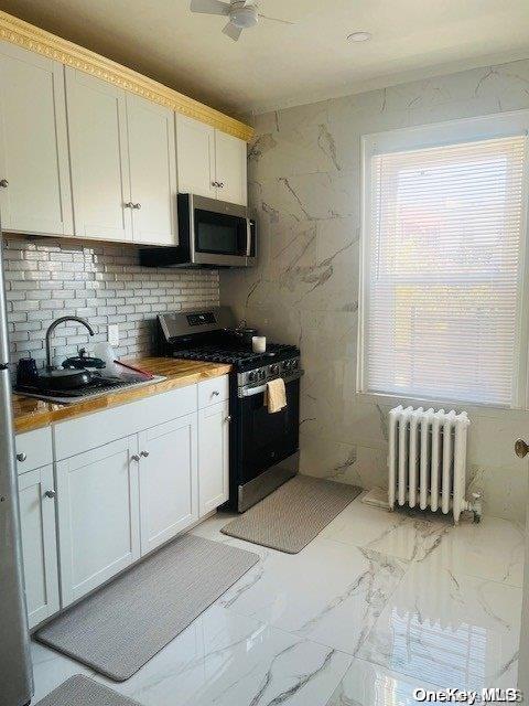 kitchen featuring stainless steel appliances, sink, white cabinets, radiator heating unit, and butcher block counters