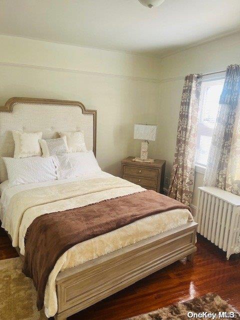 bedroom with dark hardwood / wood-style floors and radiator heating unit