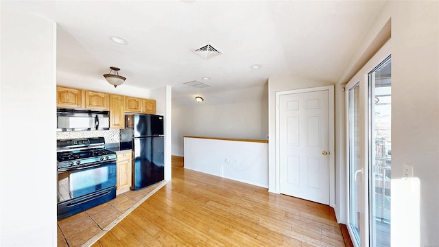 kitchen featuring light wood-type flooring, light brown cabinetry, tasteful backsplash, and black appliances