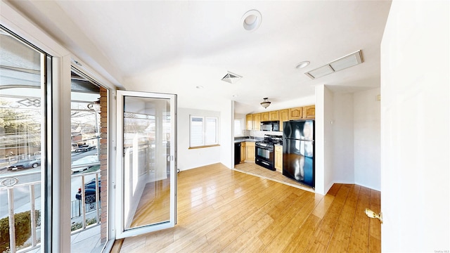 kitchen featuring light hardwood / wood-style floors, plenty of natural light, light brown cabinetry, and black appliances