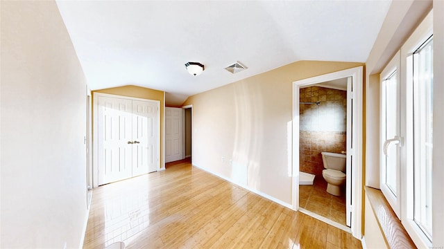 unfurnished bedroom featuring vaulted ceiling, connected bathroom, and light hardwood / wood-style floors