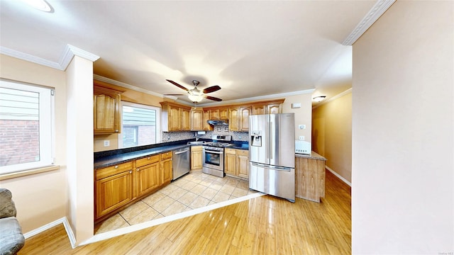 kitchen with appliances with stainless steel finishes, decorative backsplash, light wood-type flooring, ceiling fan, and crown molding