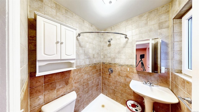 bathroom with toilet, backsplash, tiled shower, tile walls, and sink