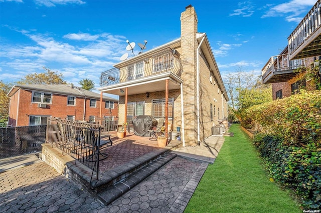 rear view of property featuring a yard, a balcony, and a patio