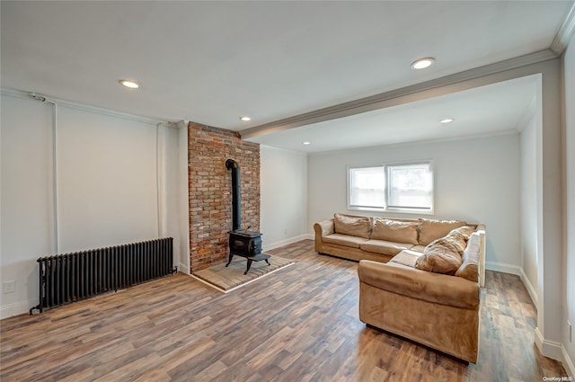 living room featuring radiator heating unit, wood-type flooring, ornamental molding, and a wood stove