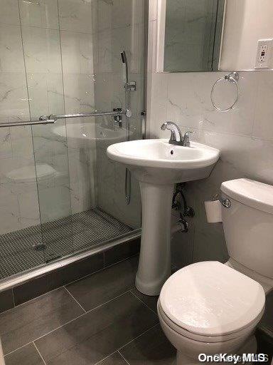 bathroom featuring tile patterned flooring, a shower with shower door, tile walls, and toilet