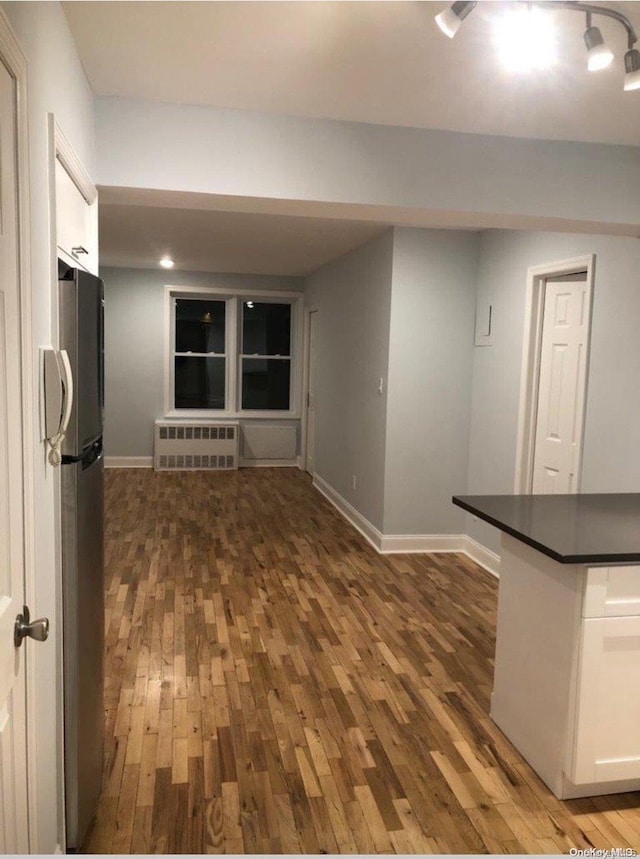 kitchen with hardwood / wood-style floors, white cabinetry, radiator, and stainless steel refrigerator