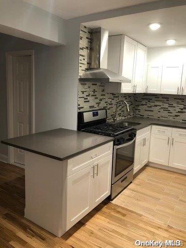 kitchen with electric range, light hardwood / wood-style floors, white cabinets, and wall chimney range hood