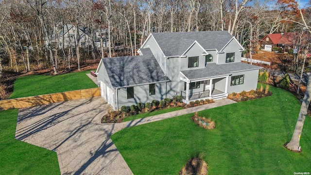 view of front of home with driveway, covered porch, roof with shingles, and a front yard