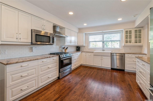 kitchen with sink, dark wood-type flooring, wall chimney range hood, white cabinets, and appliances with stainless steel finishes