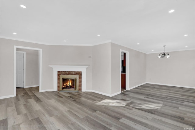 unfurnished living room with light hardwood / wood-style floors, a brick fireplace, crown molding, and a notable chandelier