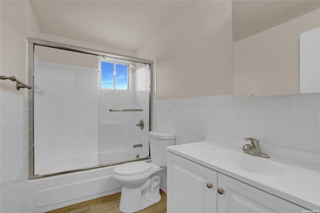 full bathroom featuring bath / shower combo with glass door, vanity, hardwood / wood-style flooring, tile walls, and toilet