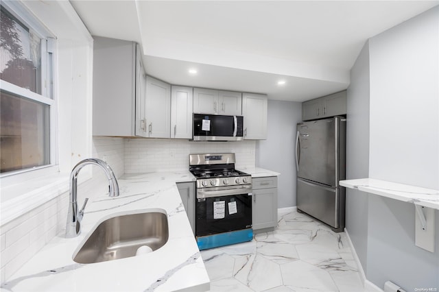 kitchen featuring sink, gray cabinets, appliances with stainless steel finishes, tasteful backsplash, and light stone counters