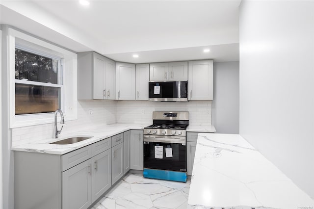 kitchen with light stone countertops, sink, tasteful backsplash, gray cabinets, and appliances with stainless steel finishes