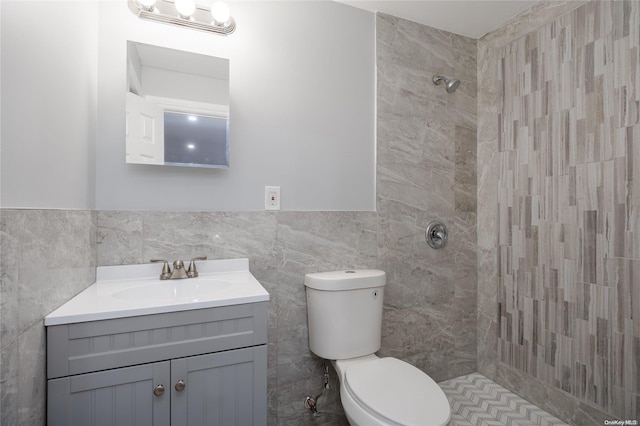 bathroom with vanity, toilet, a tile shower, and tile walls