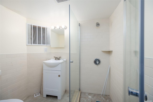 bathroom featuring tile patterned flooring, vanity, a shower with door, and tile walls