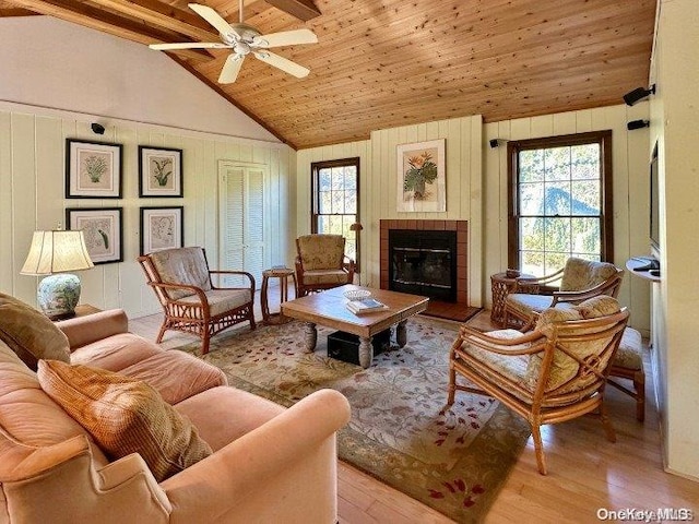 living room featuring lofted ceiling with beams, a healthy amount of sunlight, light wood-type flooring, and a tiled fireplace