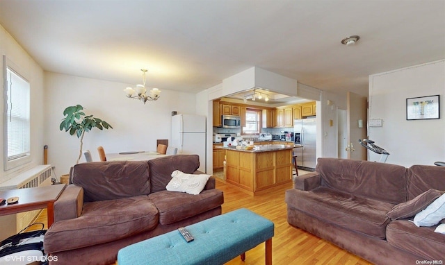 living room with radiator heating unit, light wood-type flooring, and an inviting chandelier