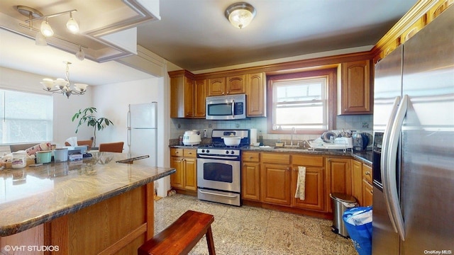 kitchen featuring backsplash, an inviting chandelier, hanging light fixtures, sink, and appliances with stainless steel finishes