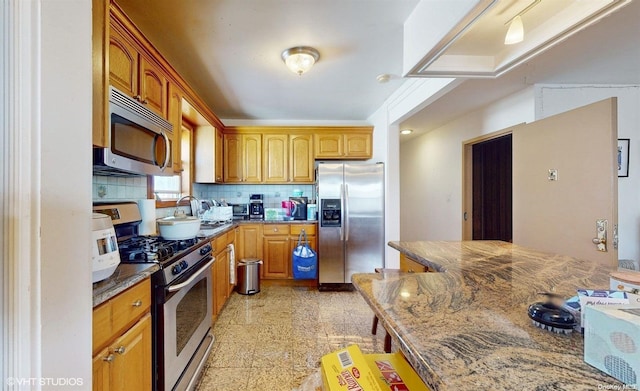 kitchen with appliances with stainless steel finishes, tasteful backsplash, dark stone counters, and sink