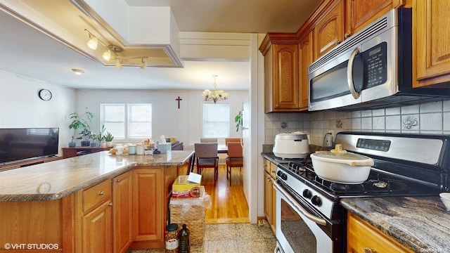 kitchen with a center island, appliances with stainless steel finishes, tasteful backsplash, a notable chandelier, and light hardwood / wood-style floors