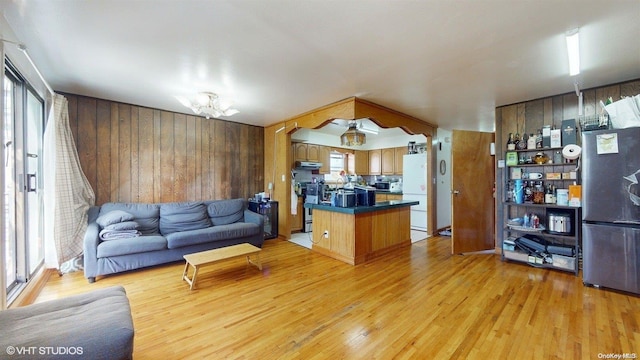 living room featuring plenty of natural light, an inviting chandelier, wooden walls, and light hardwood / wood-style flooring