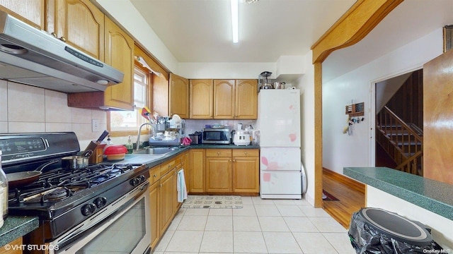 kitchen featuring sink, gas range oven, white refrigerator, backsplash, and light tile patterned floors