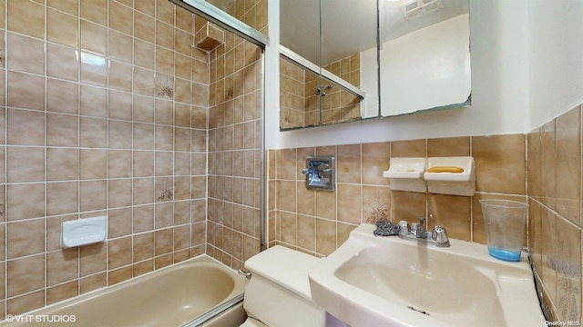 full bathroom with tiled shower / bath combo, toilet, tile walls, and sink