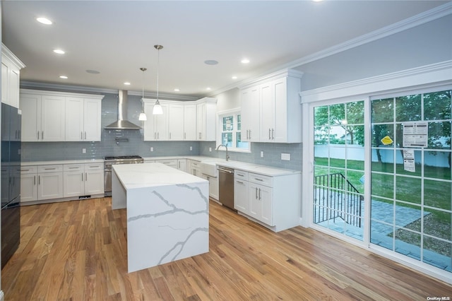 kitchen featuring wall chimney exhaust hood, a center island, stainless steel appliances, crown molding, and light wood-style floors