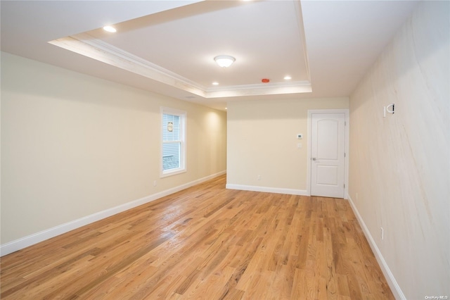 empty room featuring a tray ceiling, ornamental molding, and light wood-type flooring