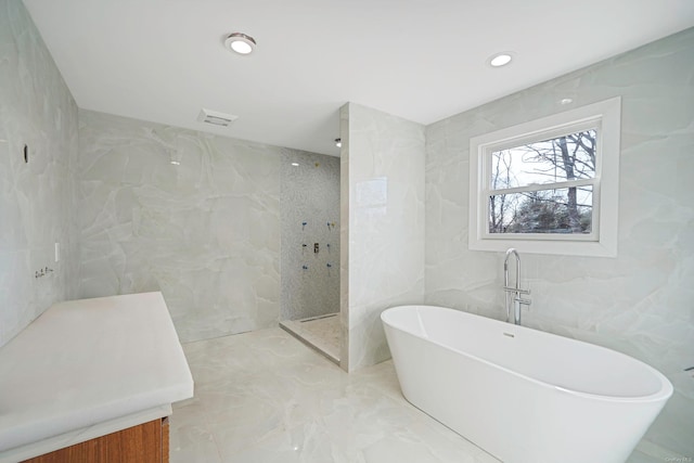 full bath with marble finish floor, tile walls, recessed lighting, a walk in shower, and a freestanding tub